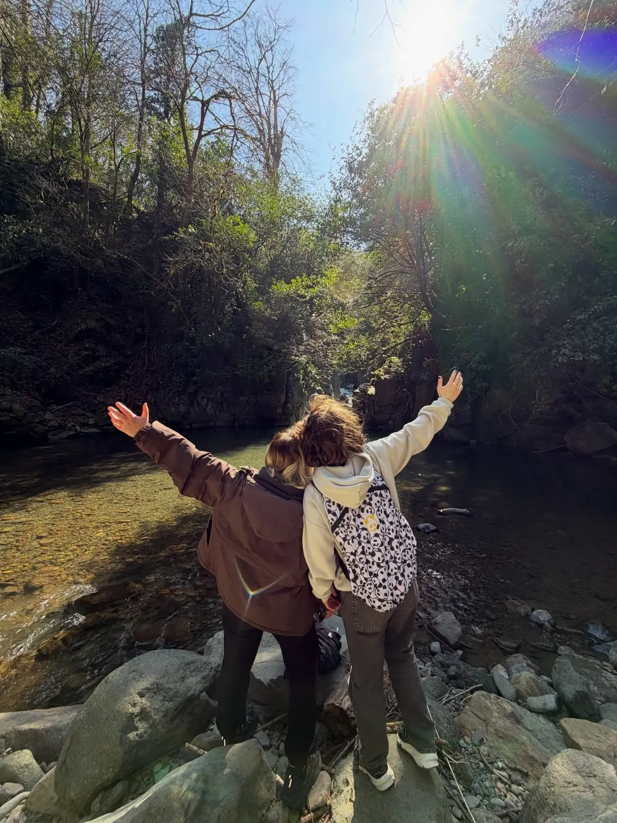 Friends with arms open by a forest river in Adjara